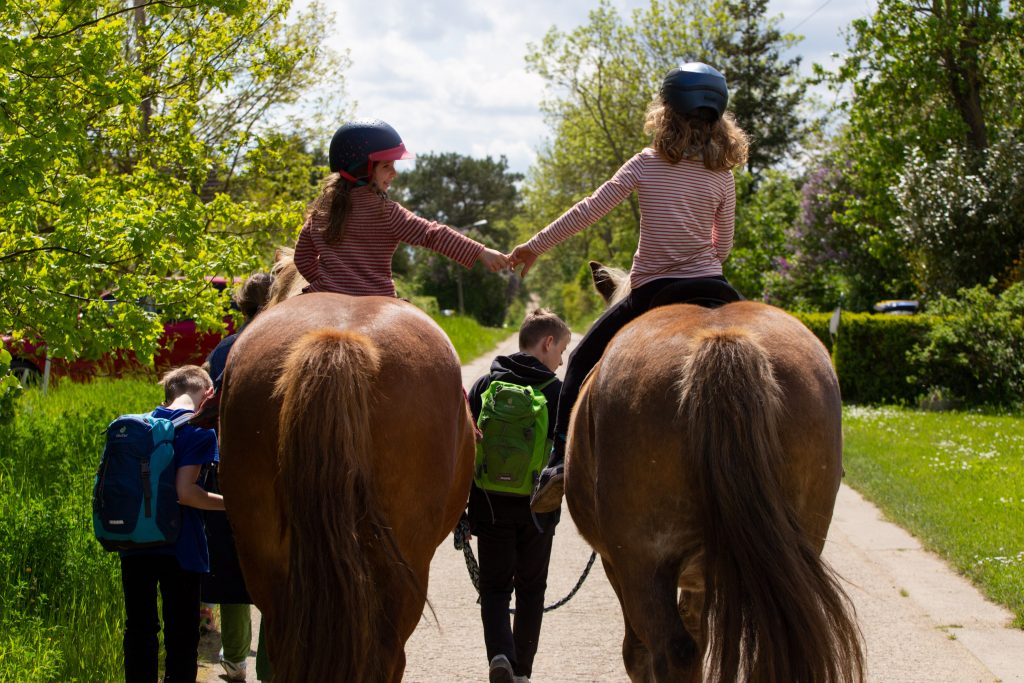 Zwei Mädchen auf Pferden händehaltend